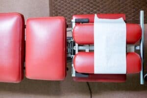Medical examination chair with red padding and paper cover for patient checkups.