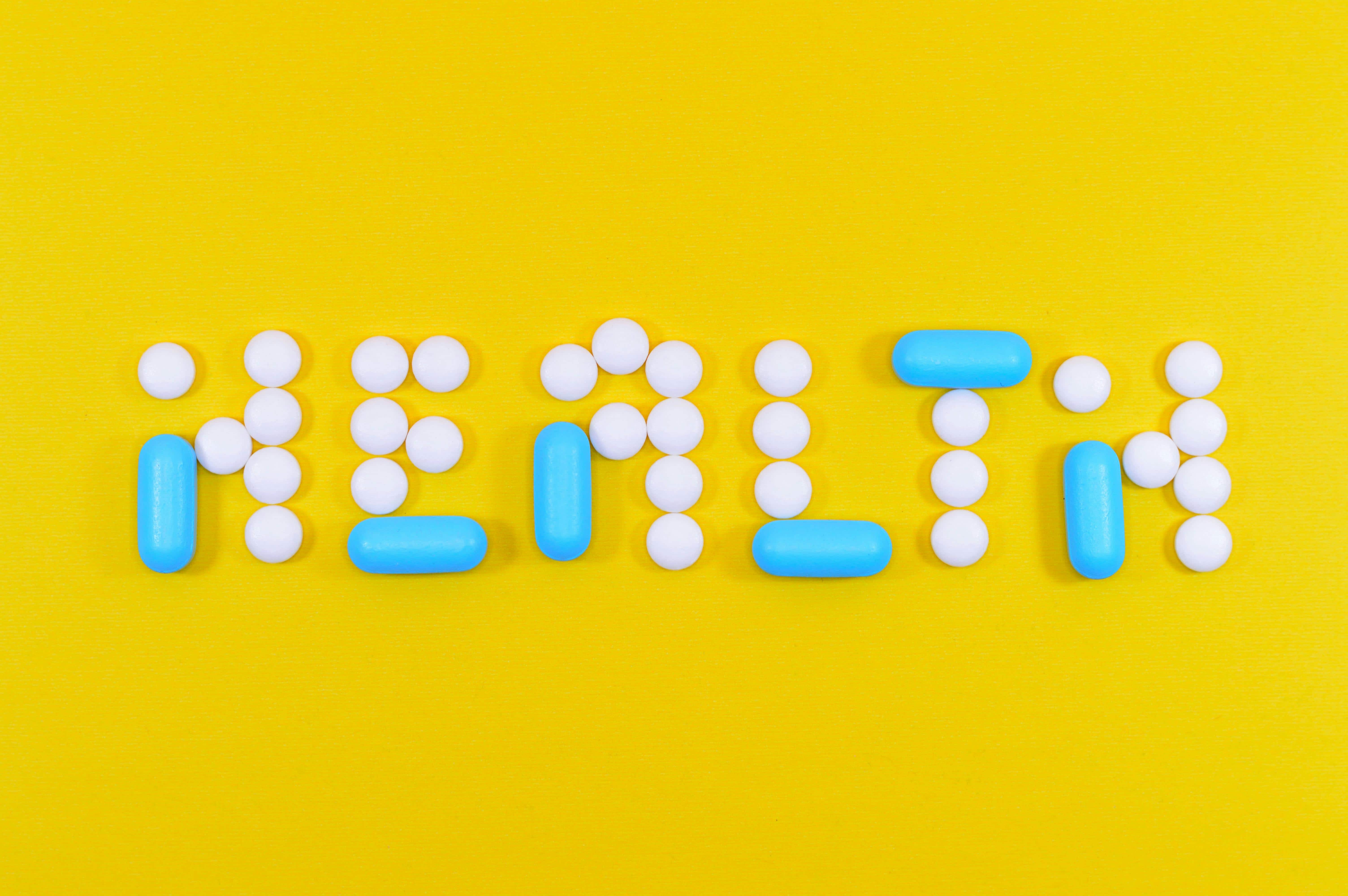 Creative pill arrangement spelling "HEALTH" on vibrant yellow background.