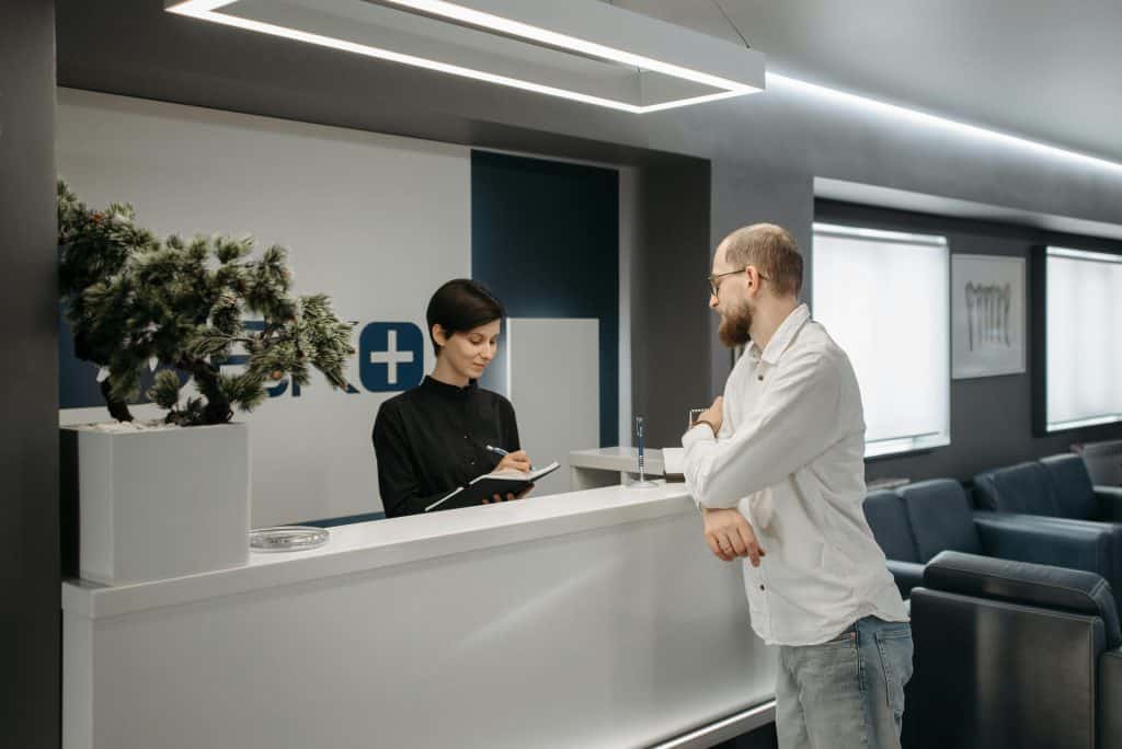 Healthcare clinic reception with staff assisting a patient at the front desk.