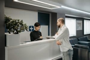 Healthcare clinic reception with staff assisting a patient at the front desk.