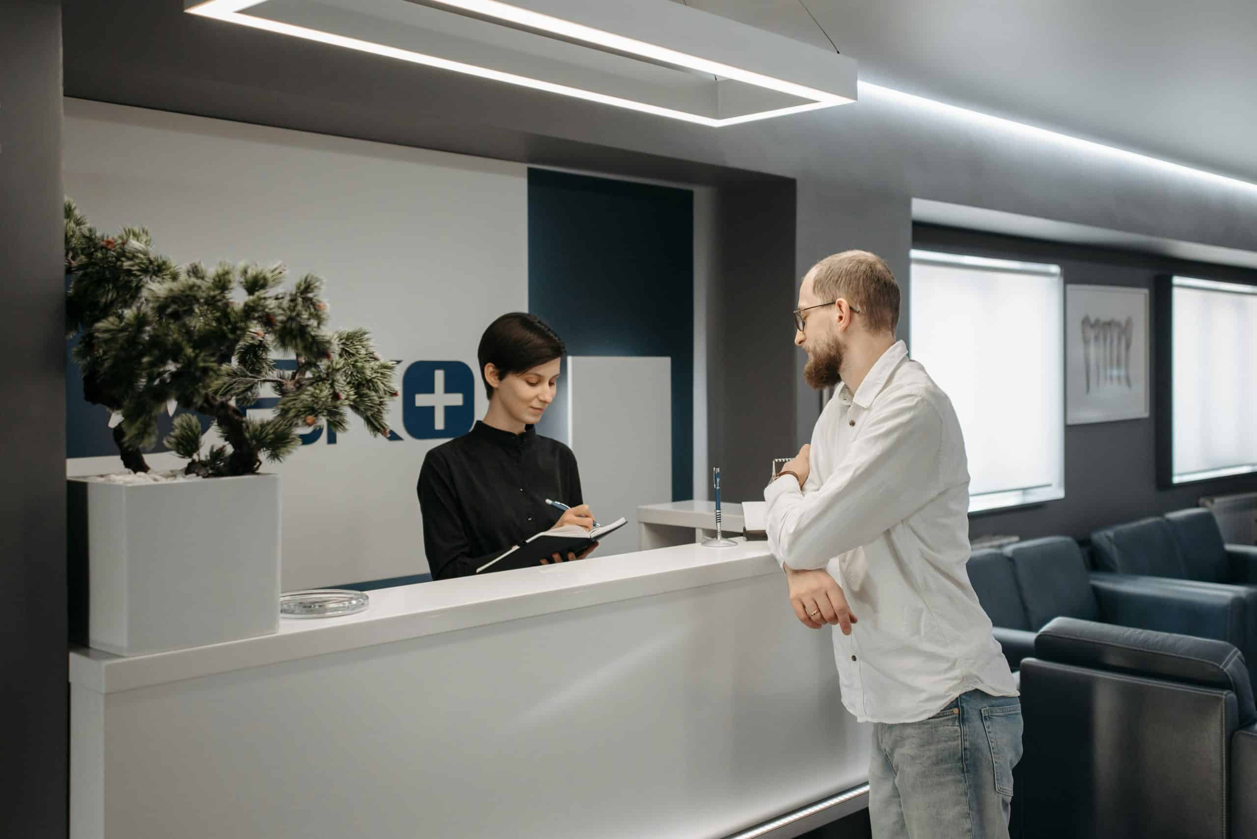 Healthcare clinic reception with staff assisting a patient at the front desk.