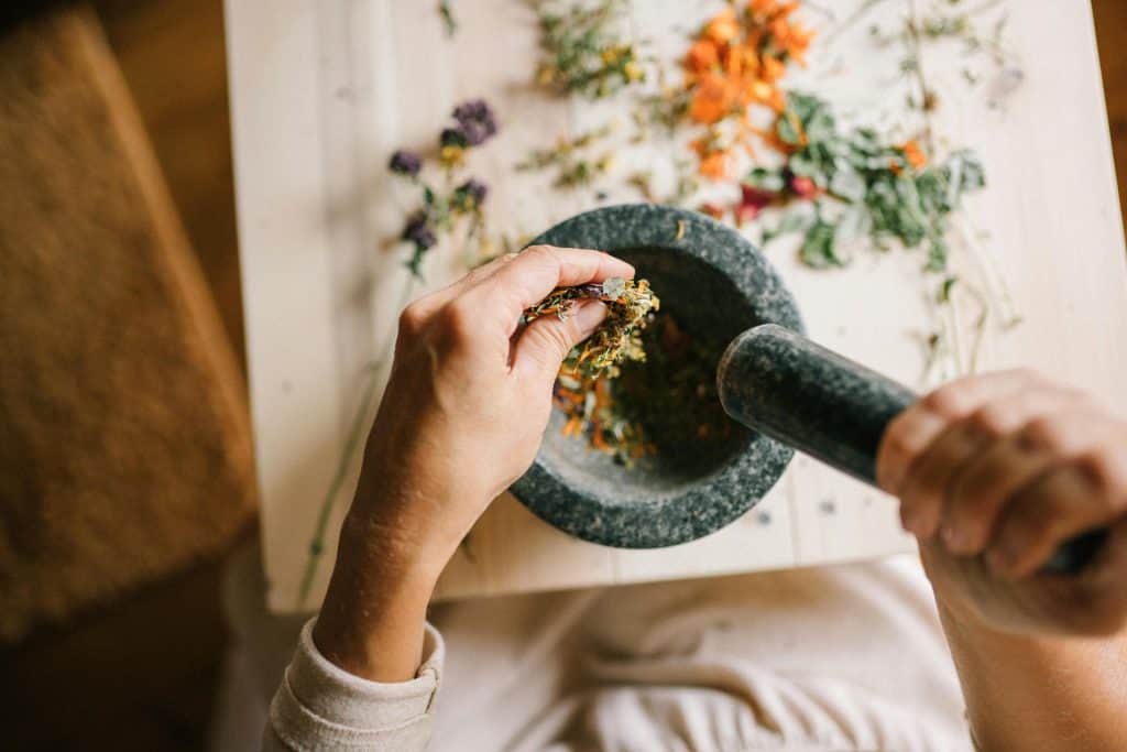 Person grinding herbs in a mortar and pestle for naturopathic remedies.