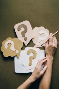 Therapist planning Google Ads with question marks and notepad for strategy.