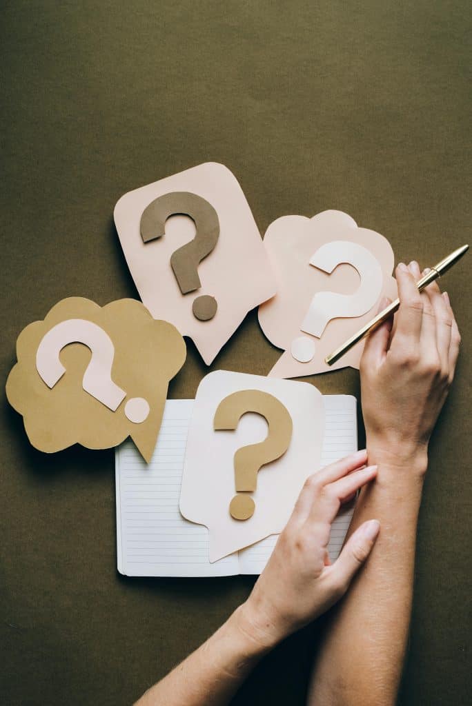 Therapist planning Google Ads with question marks and notepad for strategy.