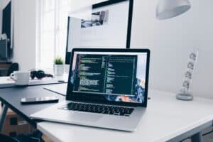Modern workspace with laptop displaying coding, monitor, and office accessories.