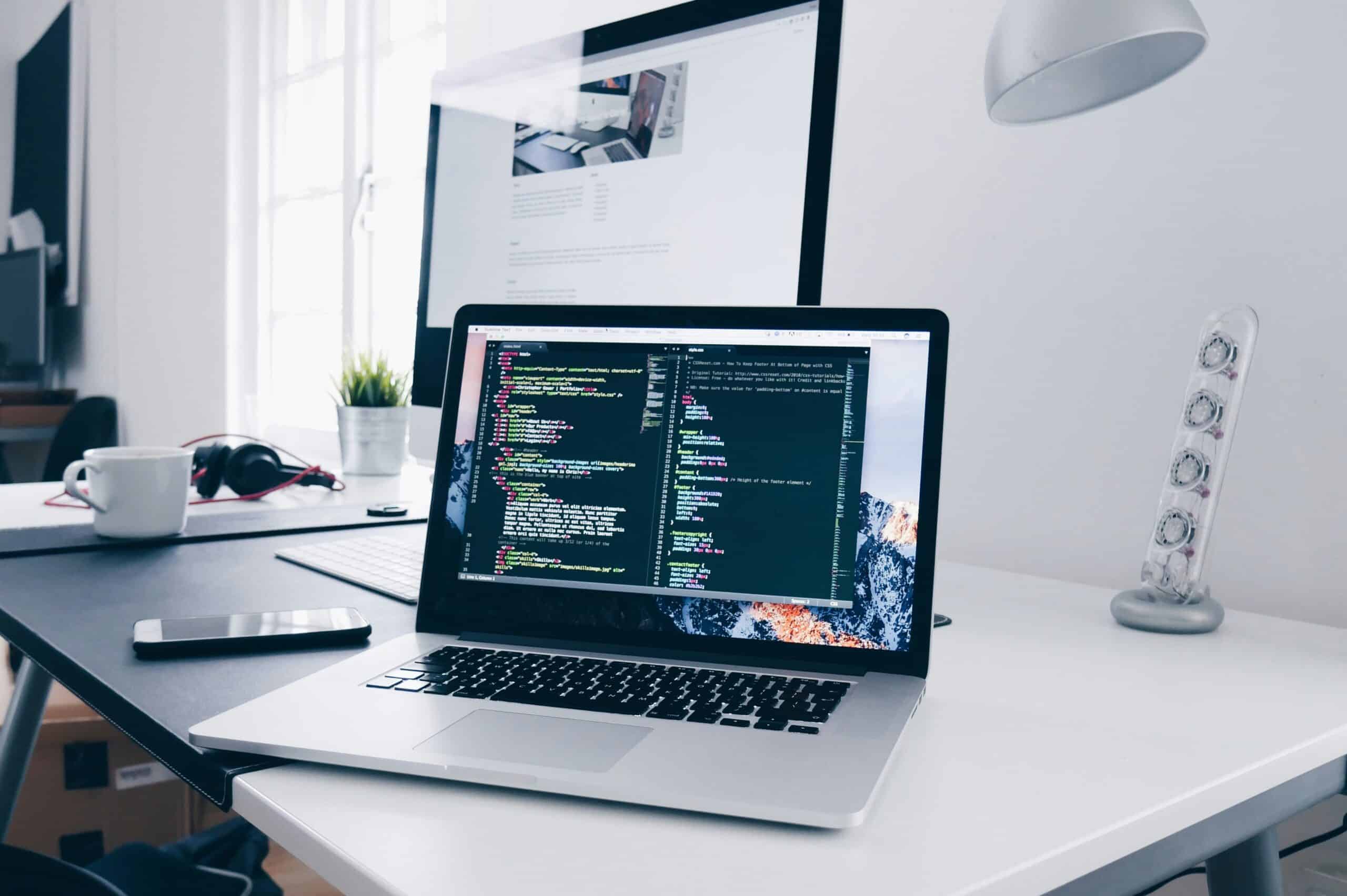 Modern workspace with laptop displaying coding, monitor, and office accessories.