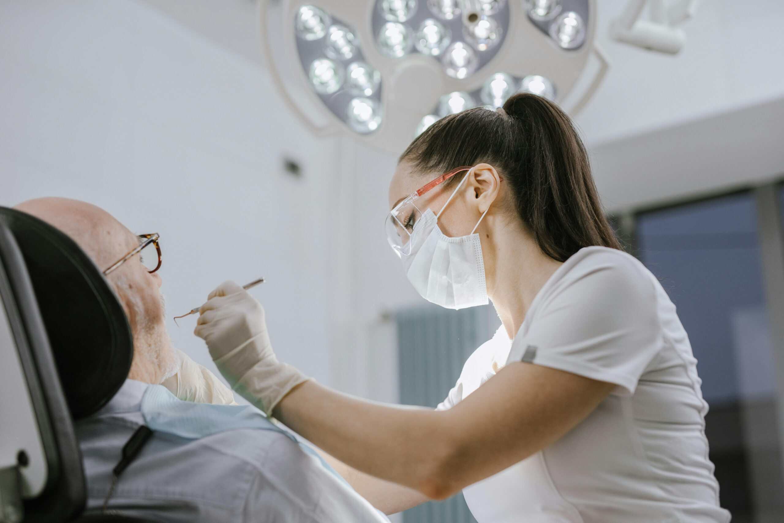 Dental professional performing oral examination on elderly patient in clinic.