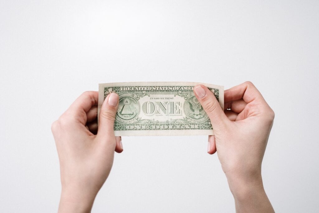 Person holding a one dollar bill with both hands against a plain background.