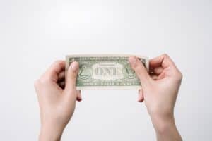 Person holding a one dollar bill with both hands against a plain background.