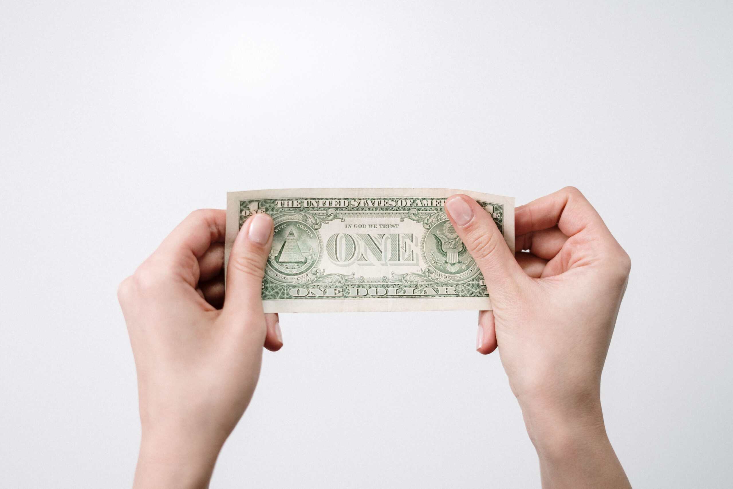 Person holding a one dollar bill with both hands against a plain background.