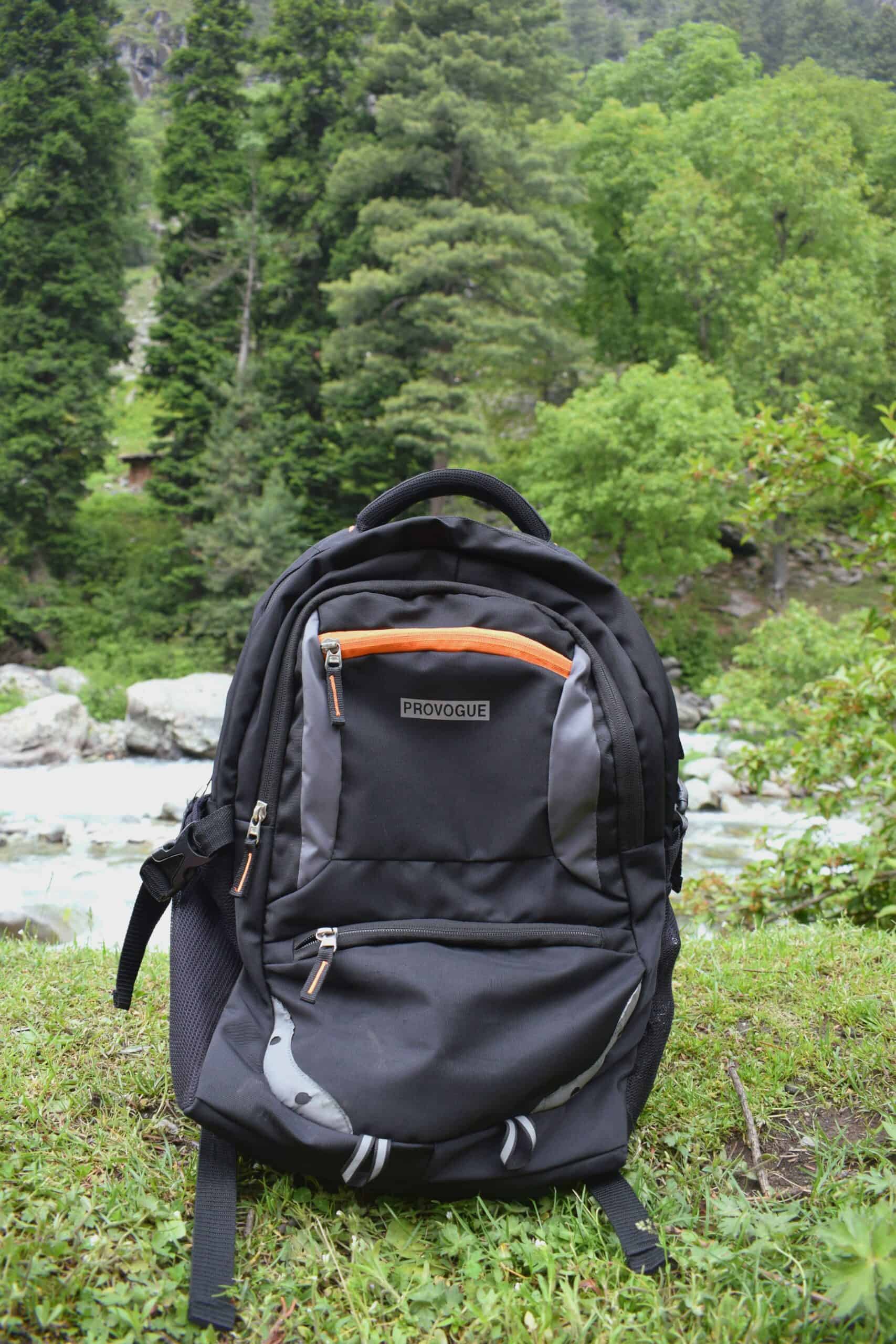 Black backpack on grass with lush green trees and river in background.