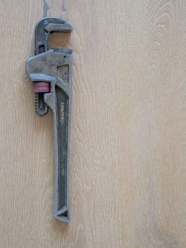 Adjustable pipe wrench on wooden surface for plumbing work.