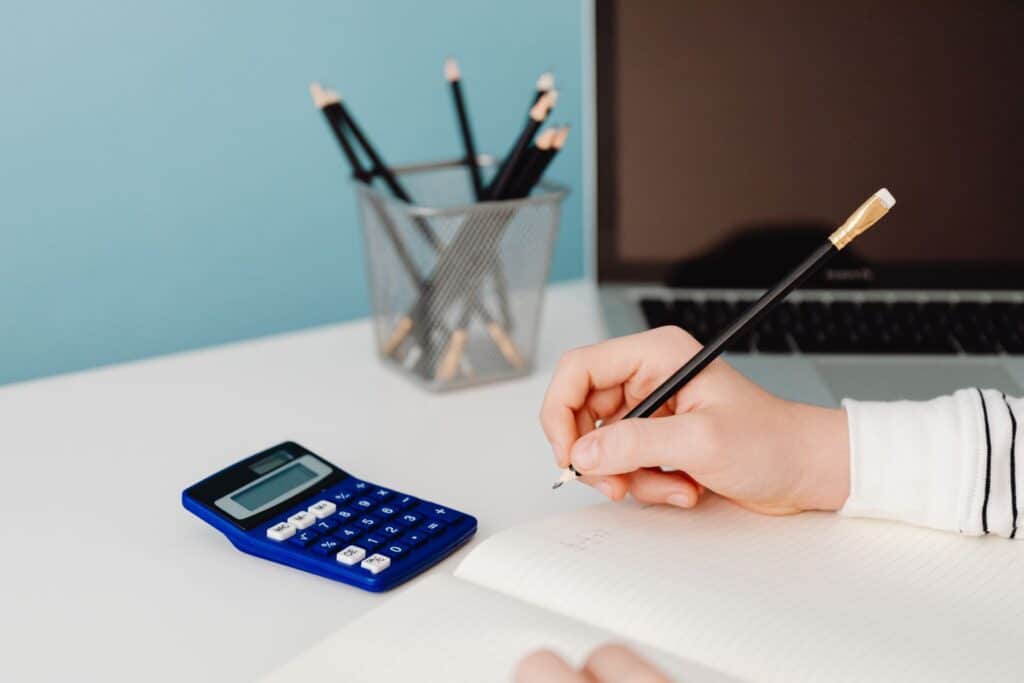 Hand writing figures in a notebook beside a calculator, working out whether Google Ads pays off for a clinic