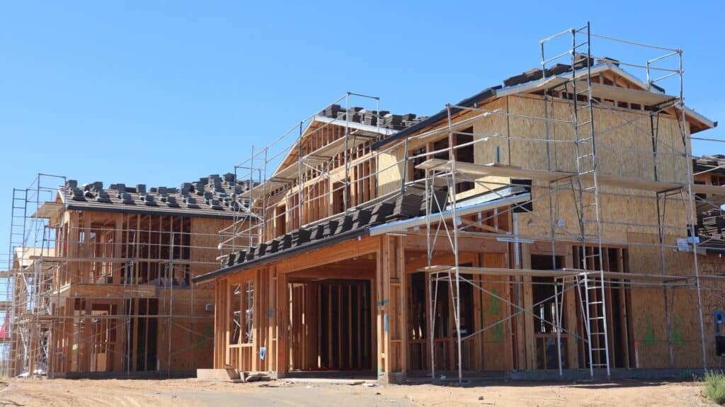 Builders framing a new custom home on a residential lot, with timber walls and roof trusses going up