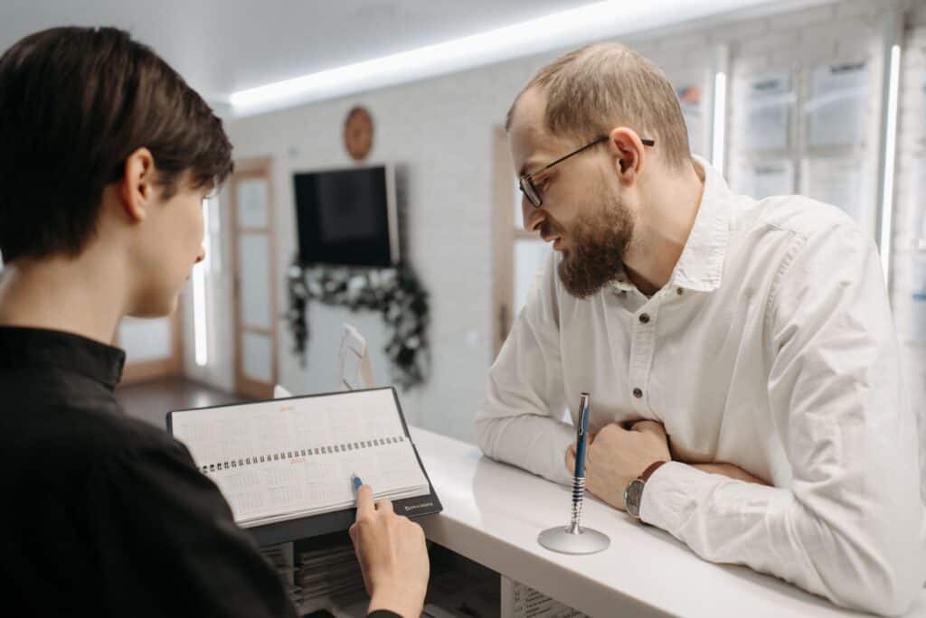 Clinic receptionist showing a patient the appointment calendar at the front desk